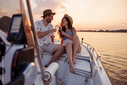 Couple making a toast and drinking champagne while sailing to the sunset on a boat