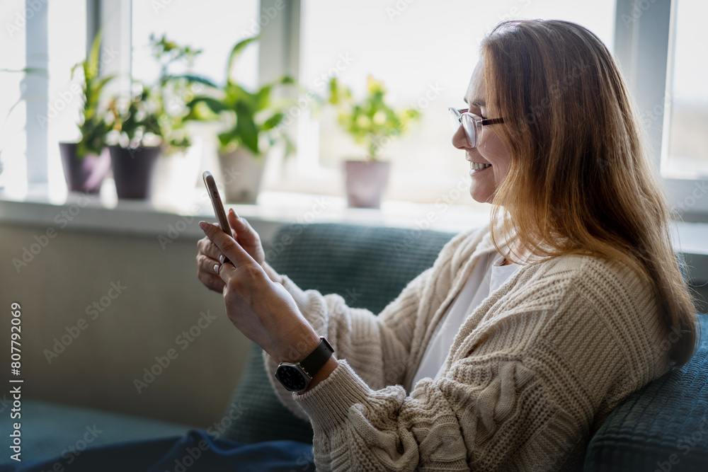 Caucasian attractive mature middle aged woman sitting on the couch at home using smartphone Caucasian attractive mature middle aged woman sitting on the couch at home using smartphone