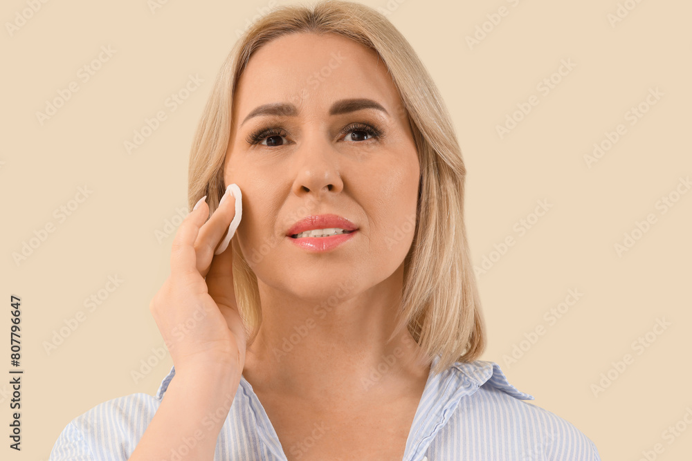 Beautiful mature woman with cotton pad on beige background Beautiful mature woman with cotton pad on beige background