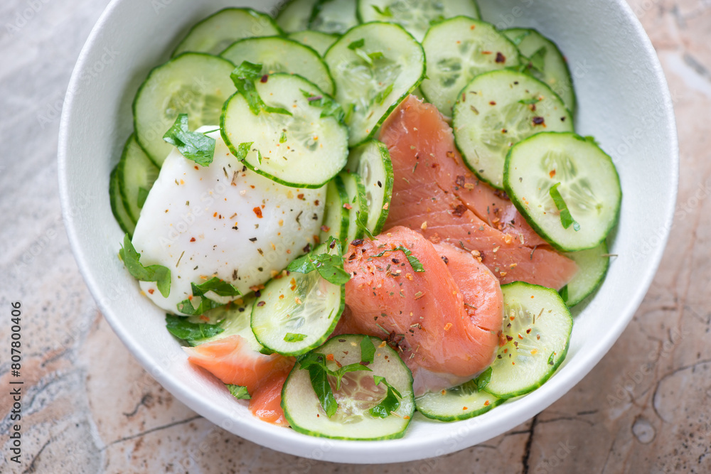 Cucumber salad with smoked salmon and poached egg in a white bowl, horizontal shot, middle closeup, selective focus Cucumber salad with smoked salmon and poached egg in a white bowl, horizontal shot, middle closeup, selective focus