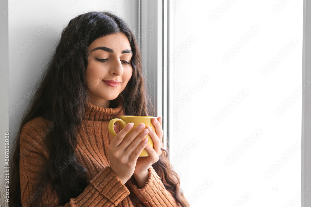 Beautiful young woman with cup of hot tea near window at home Beautiful young woman with cup of hot tea near window at home