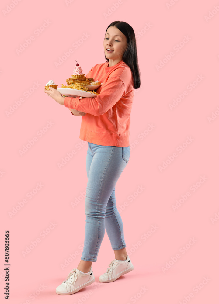 Young woman with unhealthy food on pink background. Overeating concept