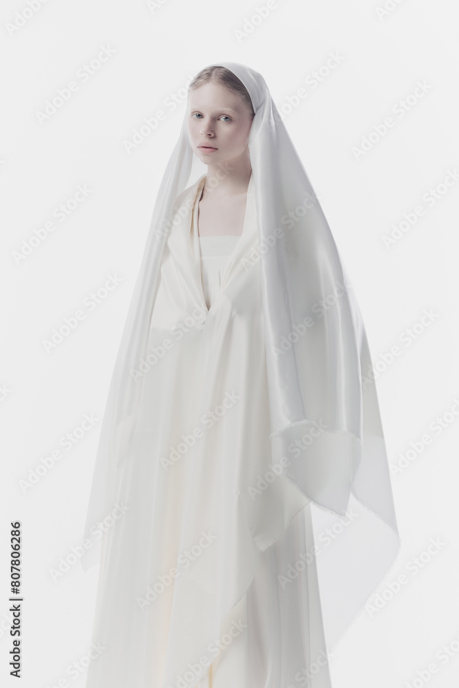 Portrait of young woman with pale skin and blonde hair looking calmly at camera, looks as nun against white studio background. Concept of history, renaissance art, comparison of eras, vintage. Portrait of young woman with pale skin and blonde hair looking calmly at camera, looks as nun against white studio background. Concept of history, renaissance art, comparison of eras, vintage.