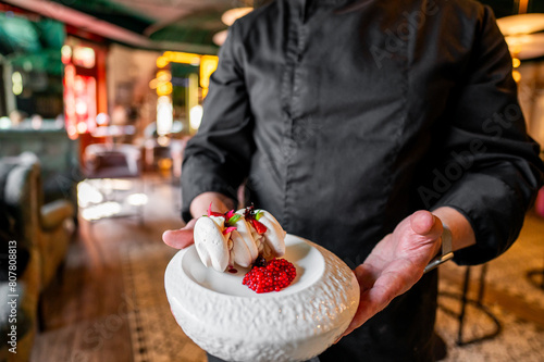 A chef elegantly presents a dessert adorned with red berries in a restaurant setting