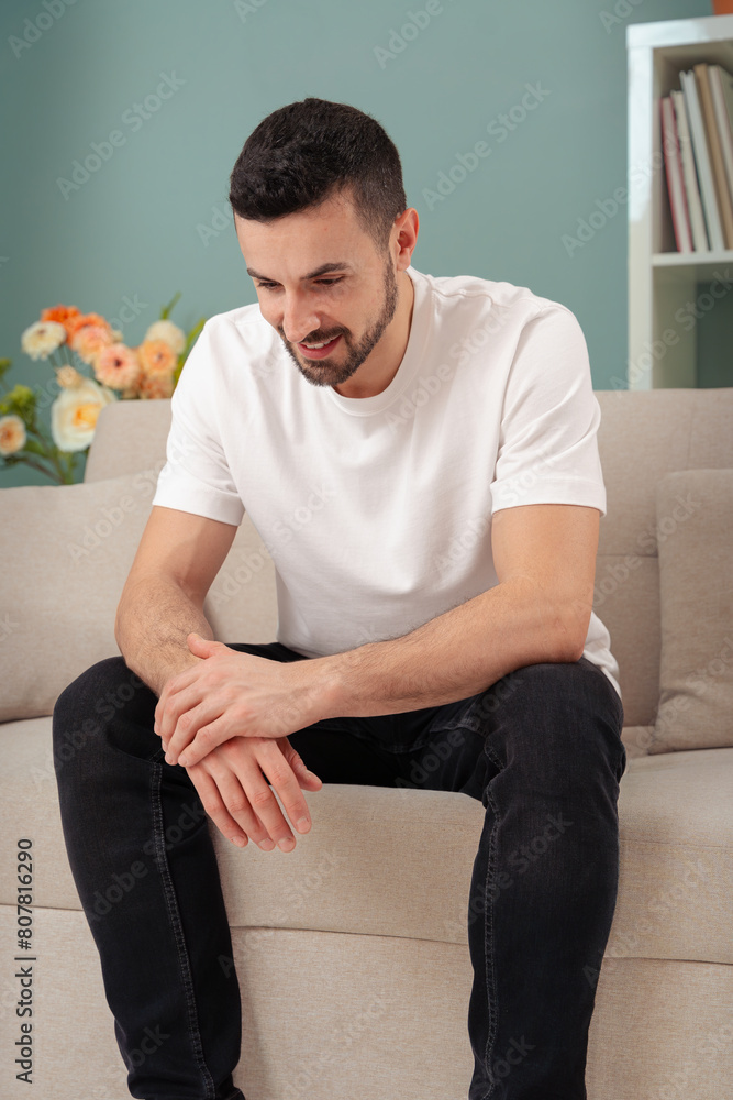 Vertical portrait caucasian man sitting on sofa and looking down thoughtfully Vertical portrait caucasian man sitting on sofa and looking down thoughtfully
