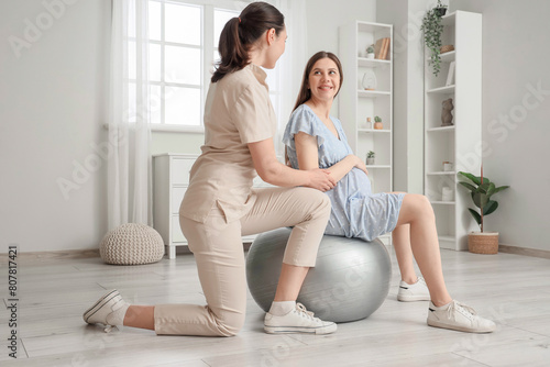 Young pregnant woman on fitball with doula training at home