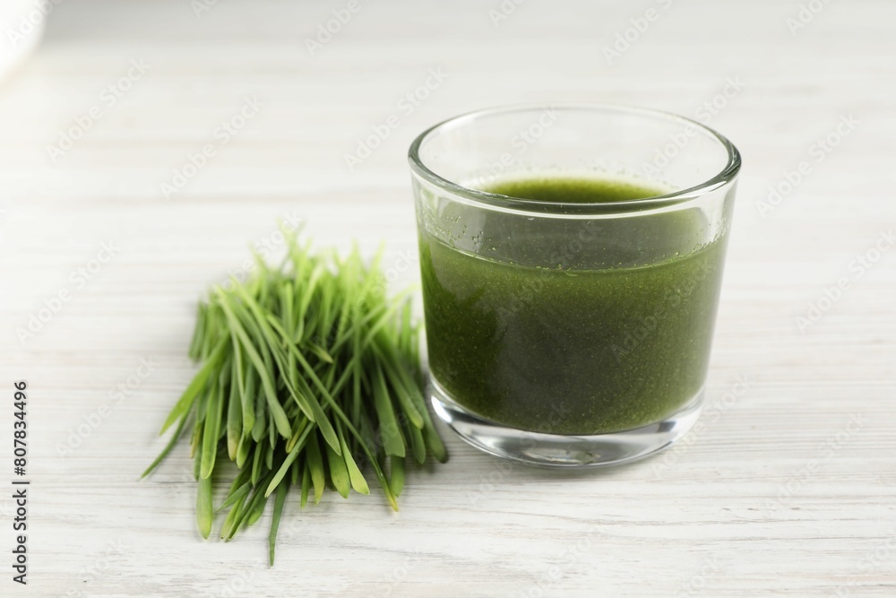 Wheat grass drink in glass and fresh sprouts on white wooden table, closeup Wheat grass drink in glass and fresh sprouts on white wooden table, closeup