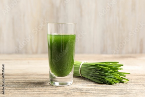 Wheat grass drink in shot glass and fresh green sprouts on wooden table, closeup