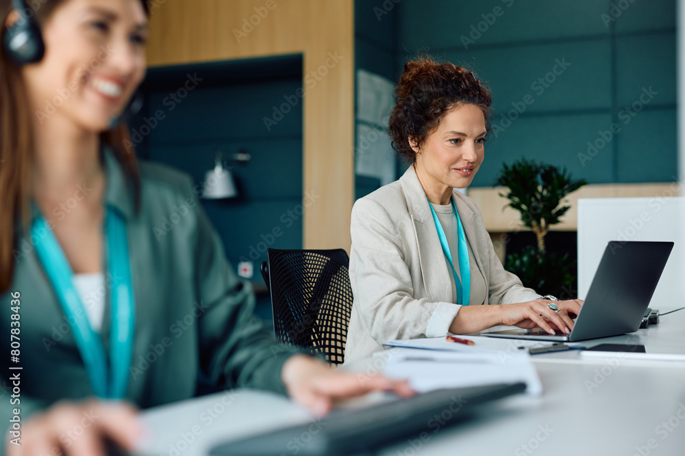 Obraz premium Smiling businesswoman working on laptop in office.