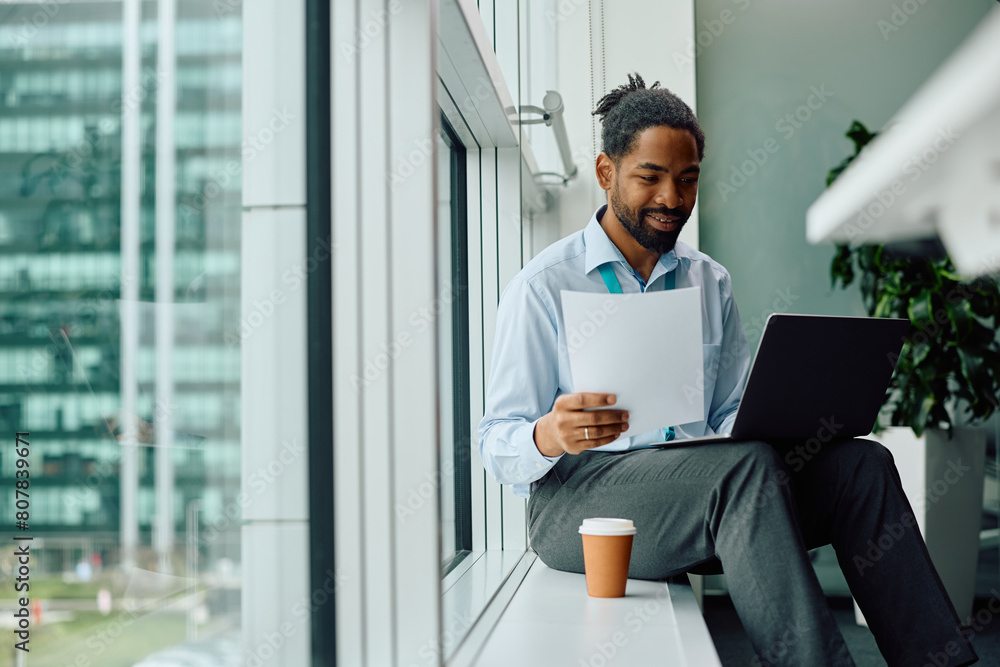 Happy black businessman working on laptop in office. Happy black businessman working on laptop in office.