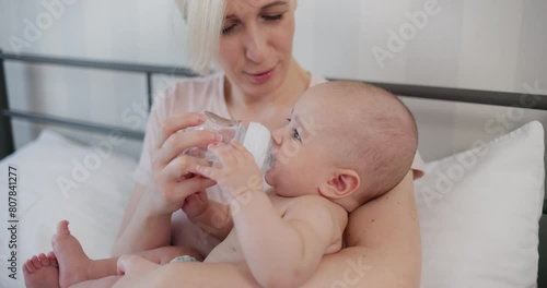  Baby drinking water from nursing bottle, sitting in his mother's arms 