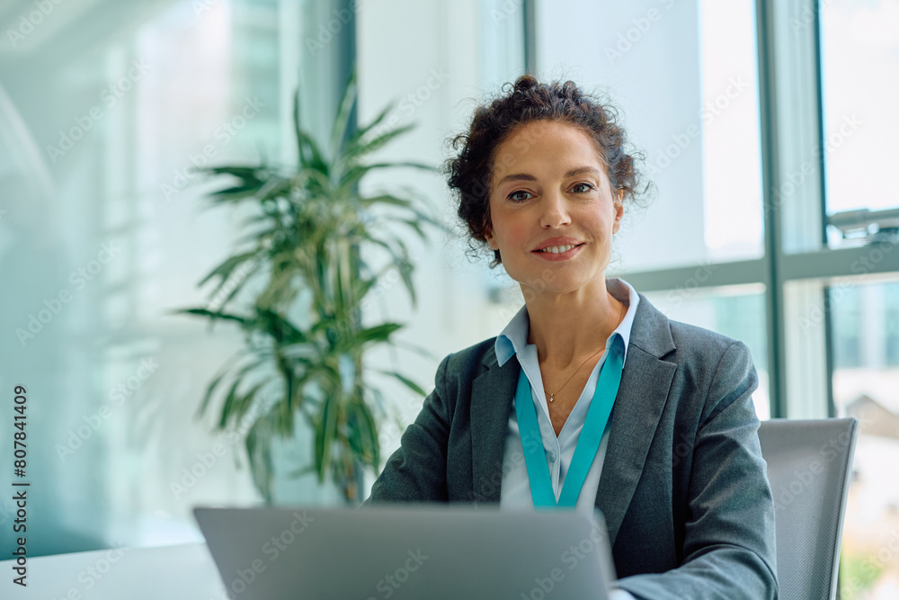 Happy financial advisor using laptop while working in her office and looking at camera. Happy financial advisor using laptop while working in her office and looking at camera.