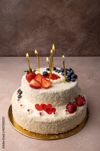 Strawberry and coconut birthday cake with cream and fresh berries. Homemade layered birthday cake with lighted candles. Selective focus, close-up.