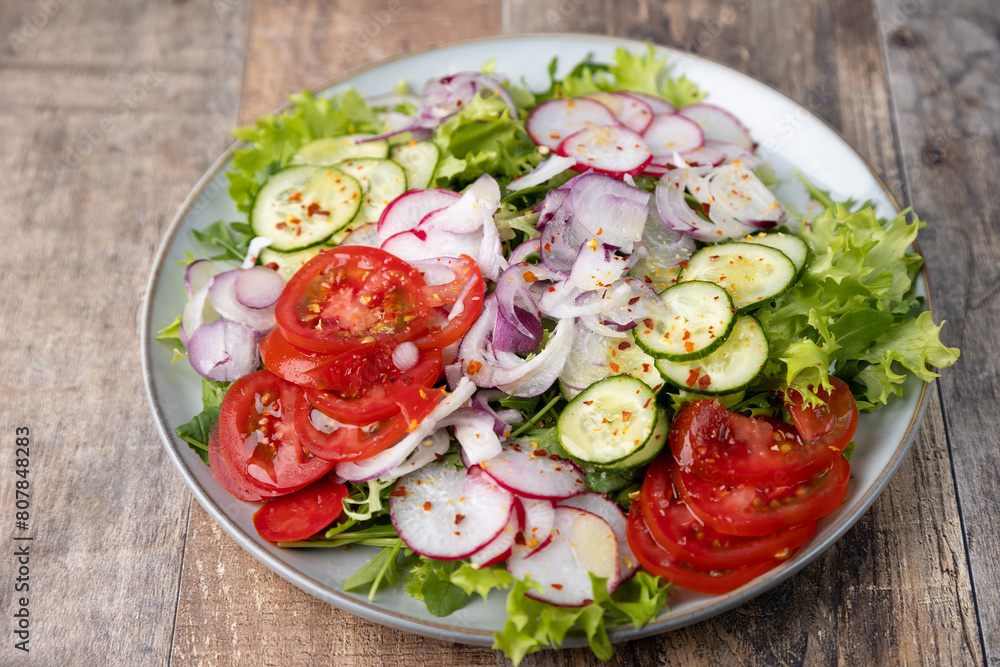 A plate of fresh chopped vegetables dressed with olive oil and spices. Vegetarian dish. Fresh vegetable salad in rustic style. Selective focus, close-up.