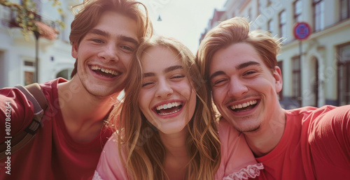 A closeup shot shows three friends taking a selfie while smiling and laughing together in the street.