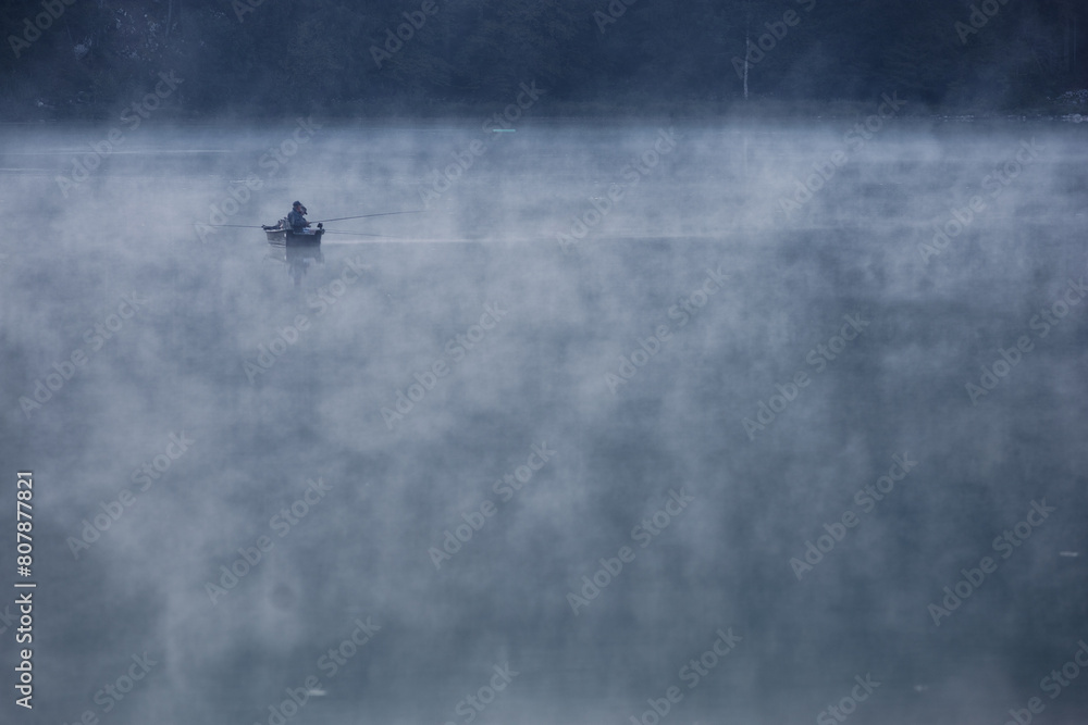 Fototapeta premium barque avec pêcheurs dans la brume matinale sur le lac Genin dans l'Ain