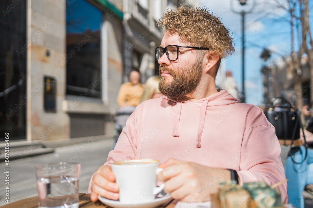 Young bearded man having breakfast at table of street cafe on spring day, drinking warm cappuccino and enjoy morning. Young bearded man having breakfast at table of street cafe on spring day, drinking warm cappuccino and enjoy morning.