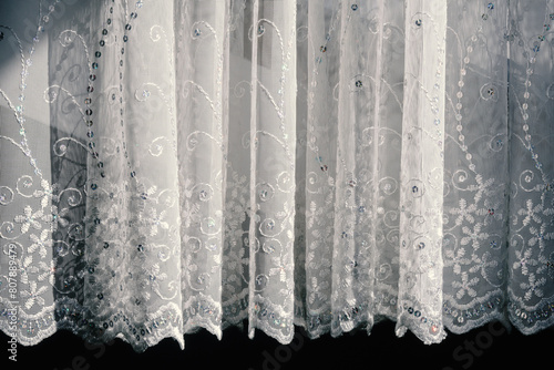 Sheer lace white pleated curtain tulle with embroidery and sequins in the rays of the sun photo