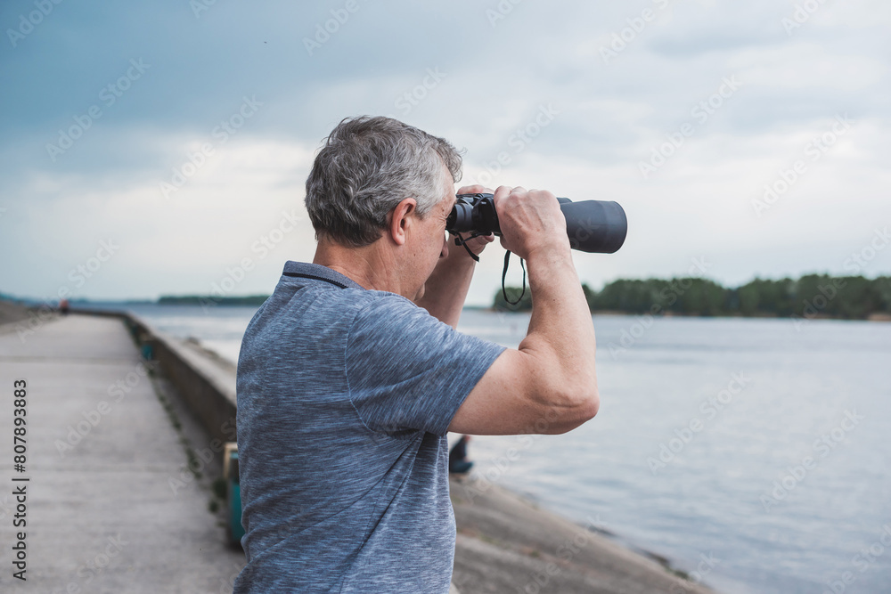 Obraz premium European Mature man looking in a binoculars . Hobby and recreation concept