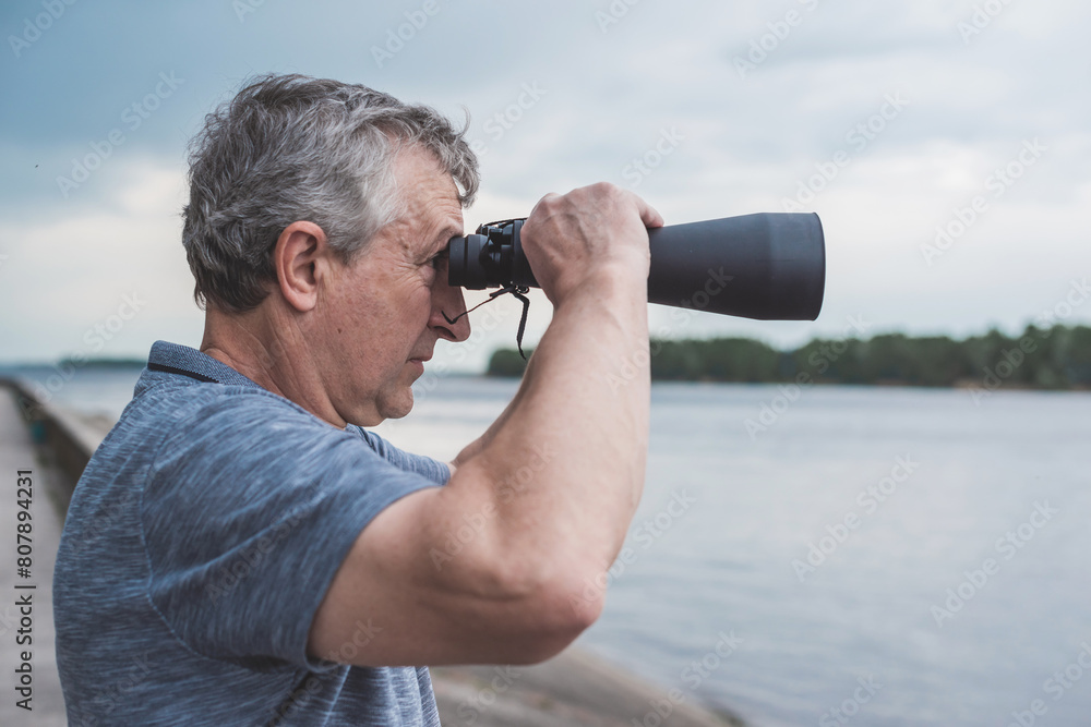 Obraz premium European Mature man looking in a binoculars . Hobby and recreation concept