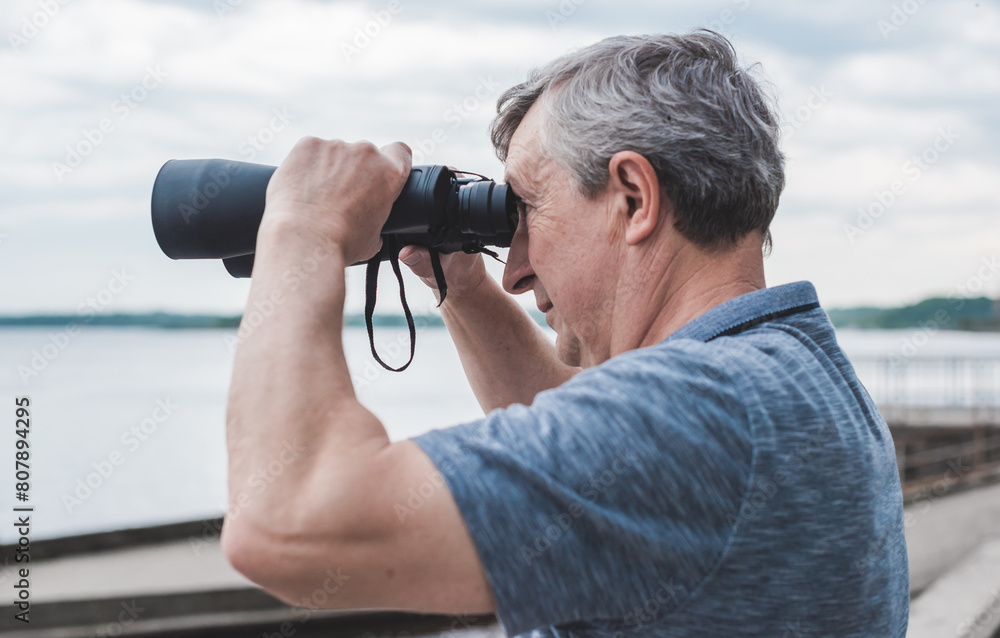 European Mature man looking in a binoculars . Hobby and recreation concept