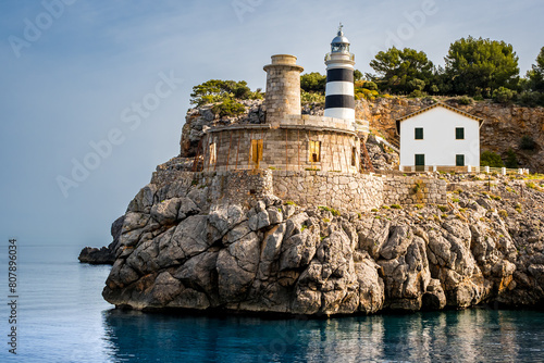 Far de sa Creu lighthouse bathed in gentle morning sunlight, graces the entrance of Port de Sóller, with old beacon ruin in foreground, capturing the beauty of Mallorca coastline and maritime heritage photo
