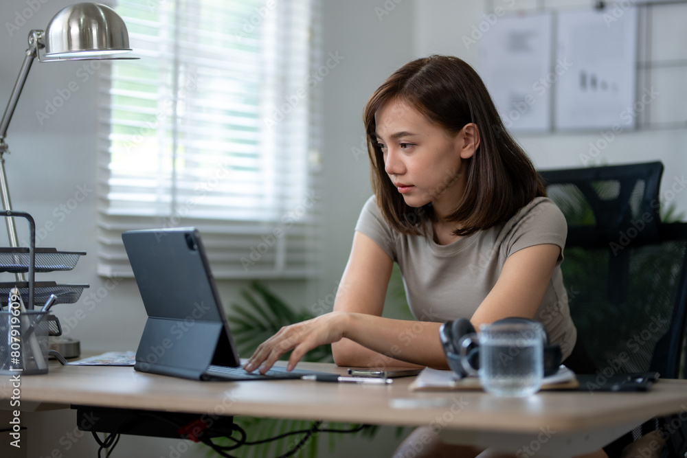 A woman is sitting at a desk with a laptop and a glass of water. She is focused on her work and she is in a serious mood A woman is sitting at a desk with a laptop and a glass of water. She is focused on her work and she is in a serious mood