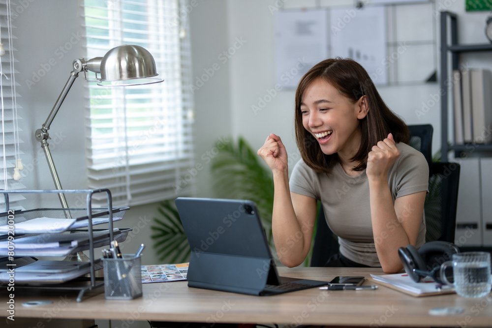 A woman is sitting at a desk with a laptop and a tablet. She is smiling and she is happy A woman is sitting at a desk with a laptop and a tablet. She is smiling and she is happy