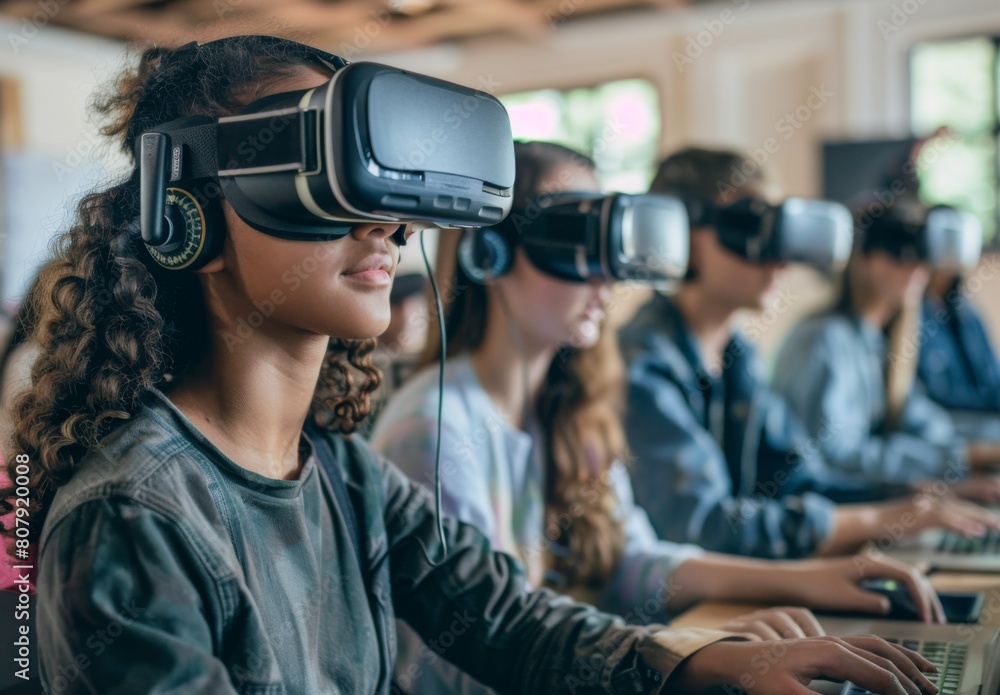 A group of students wearing VR headsets, with one student using the technology to interact and engage in an educational experience while others watch from their laptops or smartph A group of students wearing VR headsets, with one student using the technology to interact and engage in an educational experience while others watch from their laptops or smartph