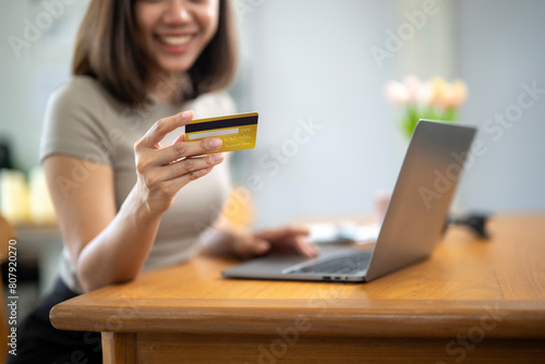 A woman is holding a credit card in front of a laptop. She is smiling and she is happy