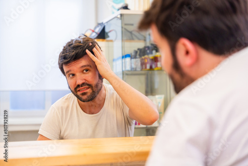 Quadro em tela Bald man with capillary prosthesis looking into hair salon mirror
