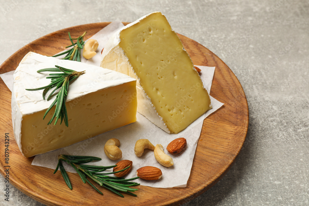 Plate with pieces of tasty camembert cheese, nuts and rosemary on grey textured table, closeup