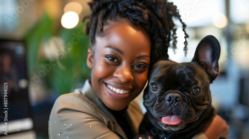 Happy african american woman cuddling French bulldog in workplace. Smiling black female businesswoman hugging holding frenchie office dog. Positive company culture & morale. Office pet photo