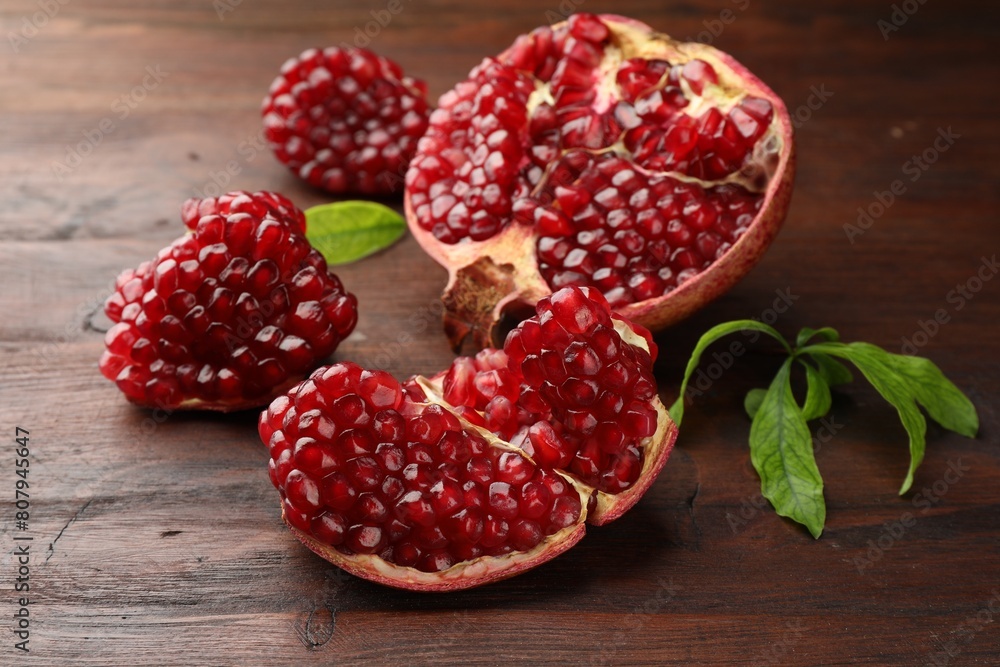 Cut fresh pomegranate and green leaves on wooden table, closeup Cut fresh pomegranate and green leaves on wooden table, closeup