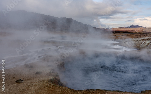 Námafjall Geothermal Area. Tourists in the distance, steaming fumaroles, boiling mud pots. Panorama of suggestive volcanic landscape. Sulfurous springs, solfataras and steam springs.