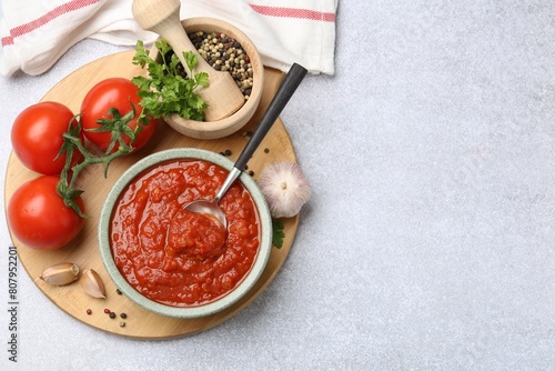 Homemade tomato sauce in bowl, spoon and fresh ingredients on light grey table, flat lay. Space for text photo