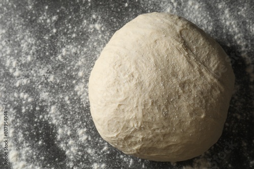 Raw homemade dough and flour on black table, top view