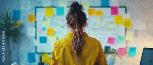 Using charts, statistics, and post-its to brainstorm a new marketing strategy, a young female entrepreneur mind maps and writes on a whiteboard in her office.