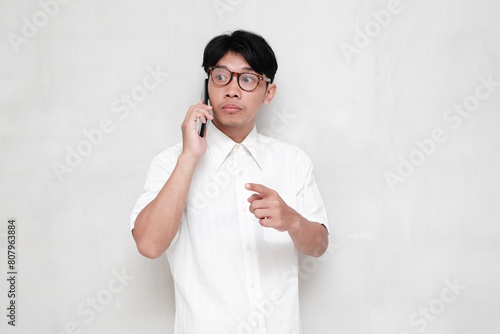 Young businessman holding mobile phone feeling bored while pointing to the side