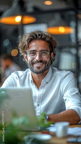 A happy businessman sitting at his desk in an office, smiling and looking into the camera with glasses on. He is wearing white shirt Smiling Businessman in Modern Office with Laptop - 4K HD Wallpaper