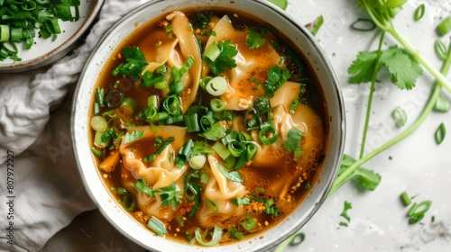 A bowl of aromatic wonton soup garnished with fresh herbs and green onions