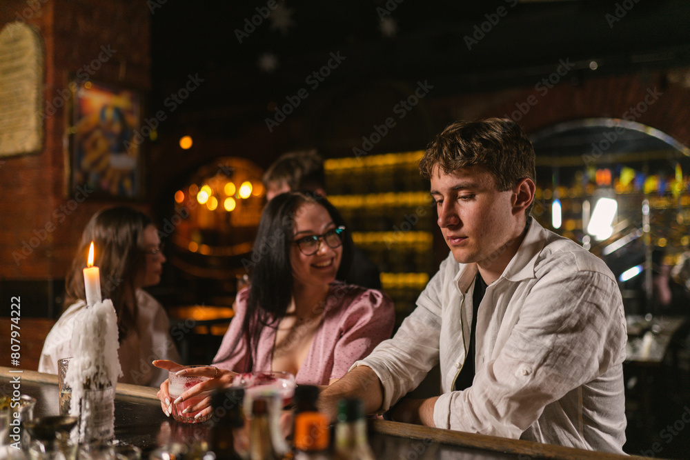Young people have rest with alcoholic beverages after hard day in bar. Smiling lady attracts attention of guy in modern restaurant