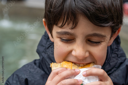 Kid eating street food lunch outdoors, bitting a sandwich. photo