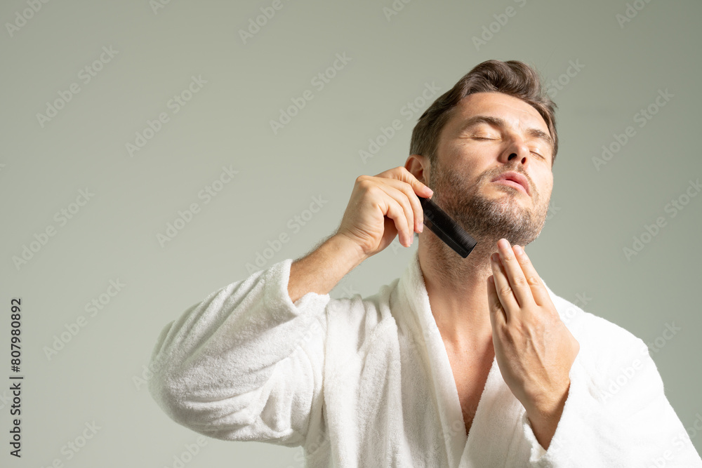 Happy handsome young shirtless man combing smooth straight hair, looking in mirror, enjoying beauty care activity, satisfied with haircare cosmetic products, haircut, barber work result Happy handsome young shirtless man combing smooth straight hair, looking in mirror, enjoying beauty care activity, satisfied with haircare cosmetic products, haircut, barber work result