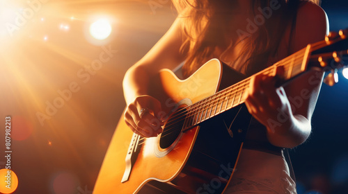 a woman's hand strumming a guitar at a concert, with the stage lights 