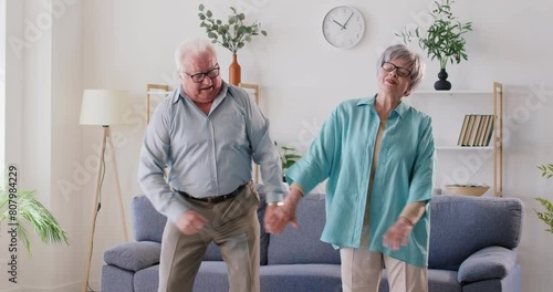 Dancing senior couple, overjoyed grey-haired husband and wife enjoy good time together at home, happy elderly spouses enjoy cool dance in living room, active healthy people moving in joy  photo