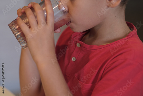 A boy enjoys a refreshing sip of water, focusing on his hands and the glass. This image encourages healthy hydration habits for children.