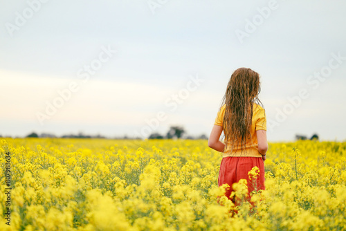 long haired girl playing in vibrant canola field in full bloom during Spring season photo