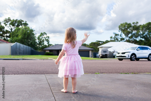 Happy little girl on driveway waving goodbye to neighbours cars photo