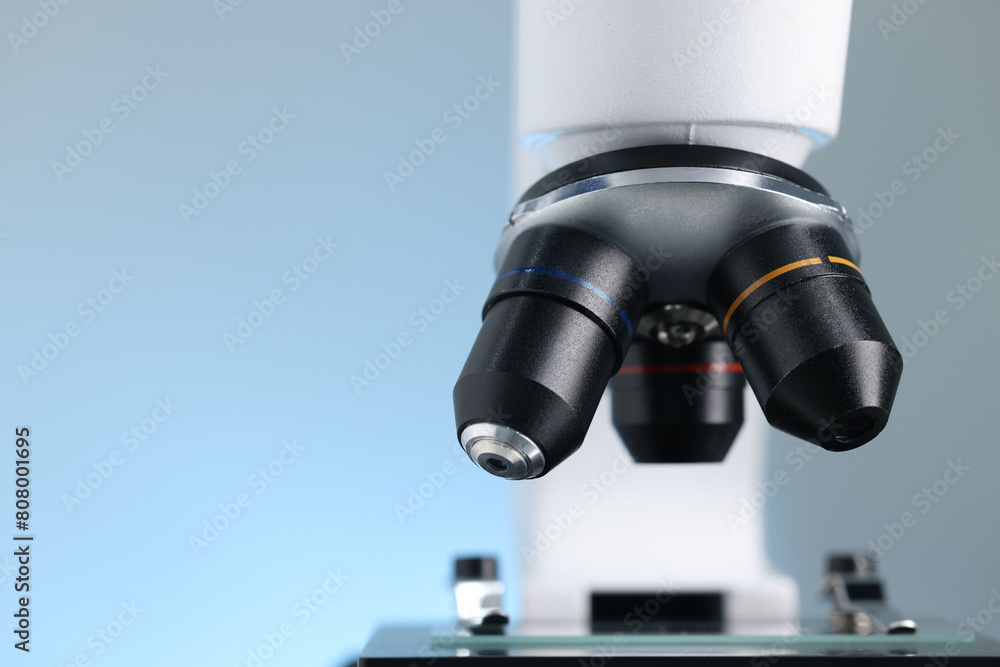 Modern microscope on light blue background, closeup view. Space for text Modern microscope on light blue background, closeup view. Space for text